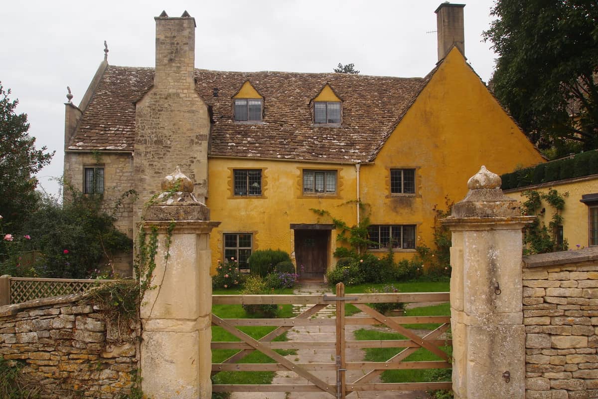 The honey-coloured front of Owlpen Manor, seen between its gate piers